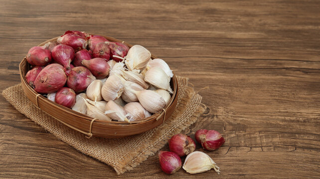 Garlic cloves and red onion or shallots on woven bamboo plate. 