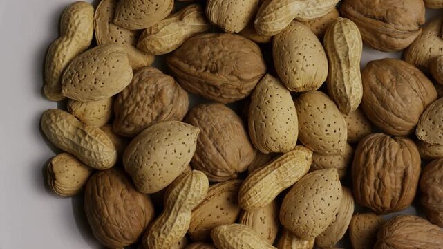 Assorted walnuts almonds and peanuts rotating on white surface