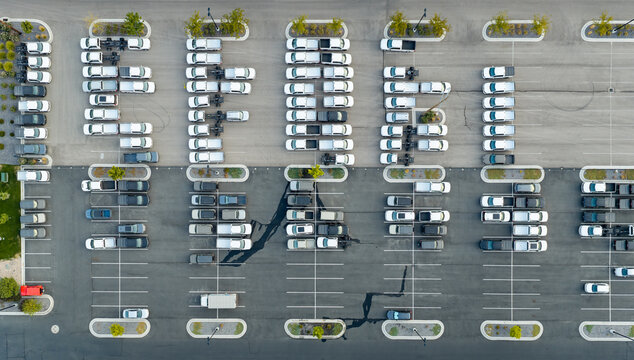 Aerial view of commercial vehicle fleet parked at a warehouse fulfillment center with rows of white trucks and vans in a large asphalt parking lot American Fork, Utah, United States.
