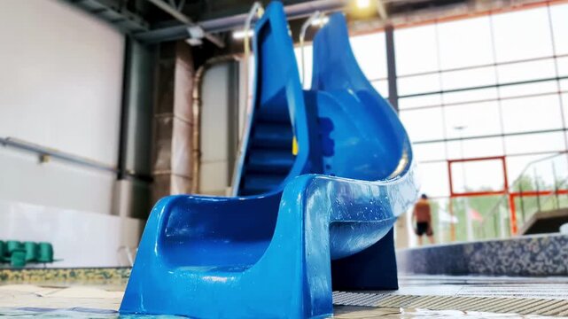 Blue water slide with water splashing into pool in modern indoor aquatic facility, empty recreational attraction structure for enjoyment and family fun