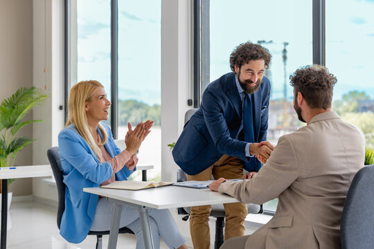 Business meeting takes place indoors with professionals shaking hands and celebrating a successful agreement