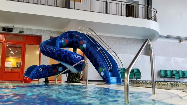 Child climbs stairs of blue snake shaped water slide and goes down into swimming pool, enjoying recreational activity at indoor water park, happy childhood moment