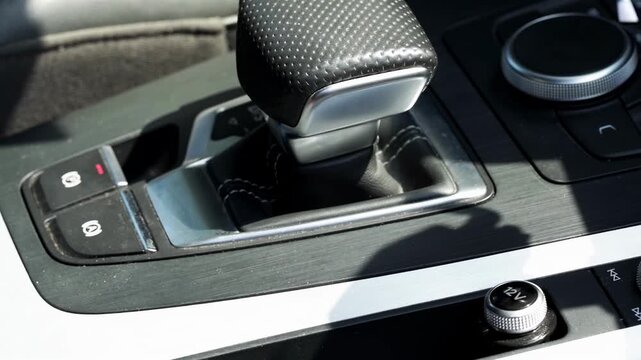 Modern car interior showing gear selector of automatic transmission in detail, highlighting perforated leather surface and surrounding controls, day light casting shadows, DSG