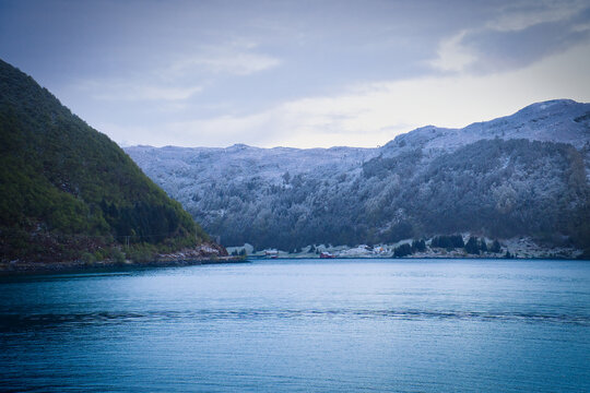 Snow-covered mountain slopes and small huts by a Nordic fjord