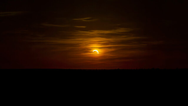 Partial solar eclipse during sunset, rare sunset with orange dramatic sky.
