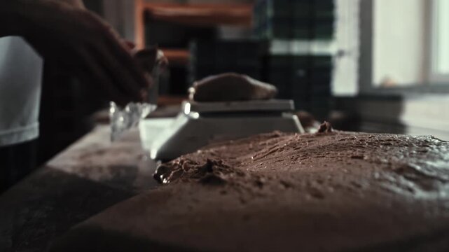 Male baker using scraper to divide large mass of dough into smaller portions weighing on scales. Part bread production process in private bakery setting. Baking ingredients preparation. Slow motion x4