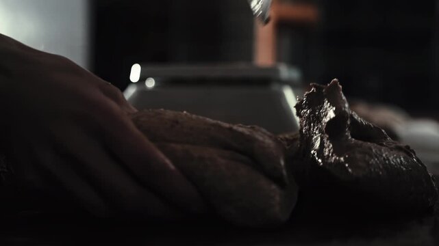 Close-up male baker hands divide dough using scraper. Dough portions prepared for weighing on scales in bakery production dark kitchen. Dark ambient lighting. Slow motion x4