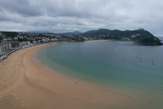 Aerial view of La Concha Bay featuring the expansive sandy beach, turquoise waters with scattered boats, and the urban coastline of San Sebastian, Basque Country, Spain.