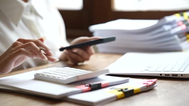 Business professional working on a laptop while managing stacks of organized documents and paperwork in a bright modern office.