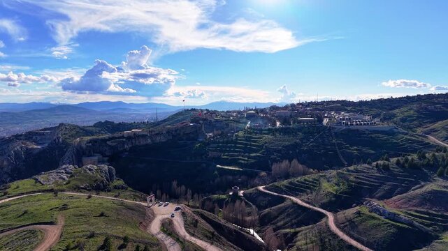 Sharp aerial movement from right to left while rising above the landscape, suddenly revealing a vast city surrounded by mountains and natural scenery.