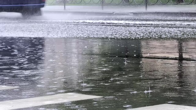 Heavy rain falling on street creating large puddles and ripples with car driving through water splashing up in slow motion city street environment