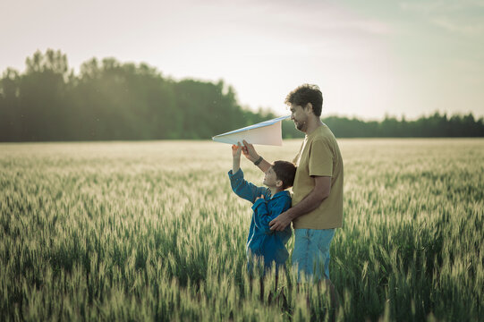 A father and son launch a paper airplane in a summer field