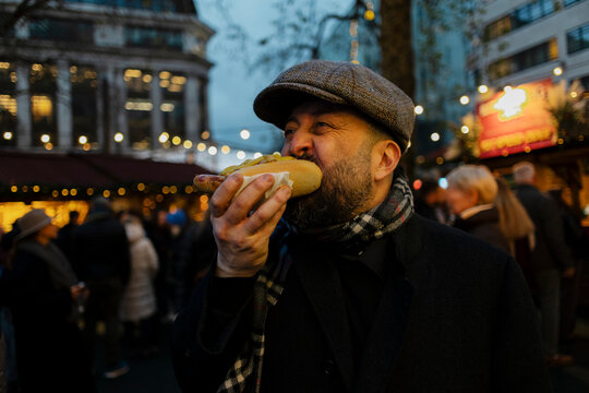 Man eats a hot dog at a festive winter market outdoors