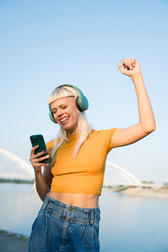 Smiling woman listening to music on headphones outdoors and dancing