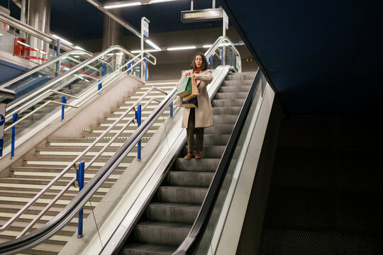 Young woman checks watch on metro escalator with shopping bags