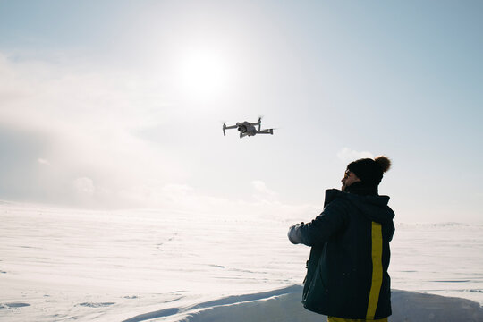 Young man flies a drone in the snowy winter landscape of Finland