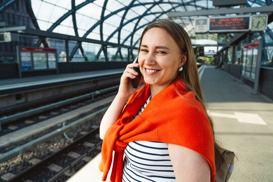 Smiling woman talking on smartphone at train station platform
