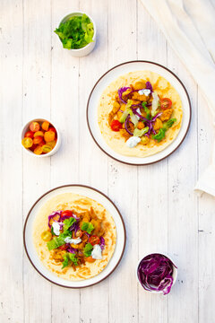A vegetarian wrap sits on a wooden table with fresh tomato and skyr