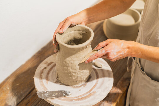 Female potter shapes clay vase on wheel in workshop