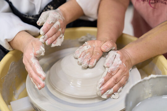Female artisan guides a student shaping clay on a pottery wheel