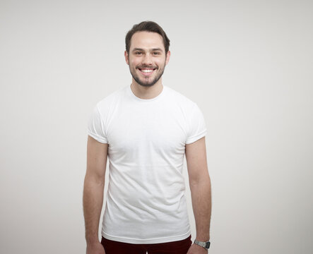 Portrait of young man standing against white background, smiling