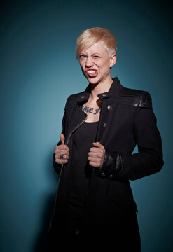Portrait of aggressive young blond woman dressed in black in front of blue background