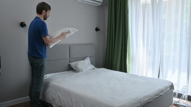 Man arranging and fluffing a white pillow on a neatly made bed