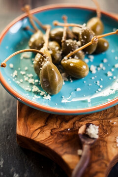 Pickled caperberries, Capparis spinosa, with sea salt on plate, studio