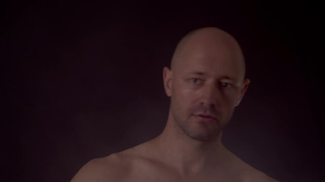 Shirtless man trying to juggle tennis balls and dropping them in dark studio. Bald male making a mistake, losing control, and dropping juggling balls in low key lighting.
