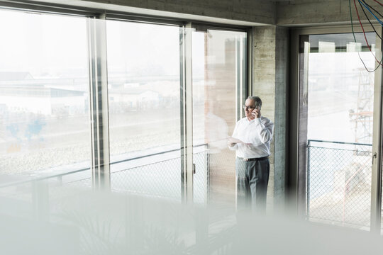 Senior manager in office standing at window, talking on the phone