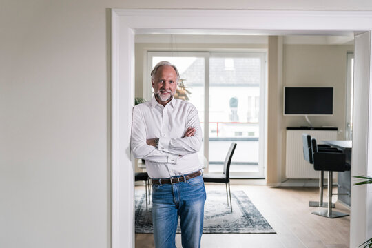 Portrait of smiling mature man leaning against door case in his apartment