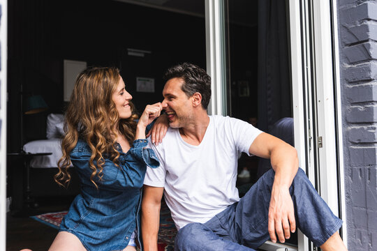 Playful couple in nightwear at home sitting at French window