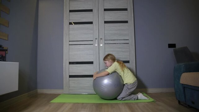 Little girl exercising with fitness ball at home. Young child performing core strength workout on stability ball indoors. Small female engaging in physical activity for health development.