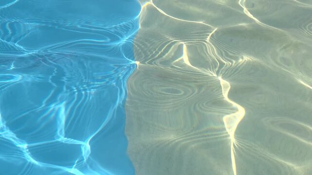 Clear water of a pool reflecting sunlight with a sandy floor on a sunny day