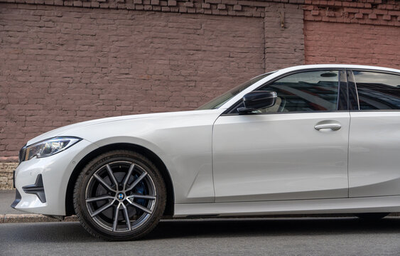 White luxury modern BMW 3 series G20 sedan car parked on an urban street side near old brick building facade, exterior view of premium german vehicle, executive transport business auto. German car. 
