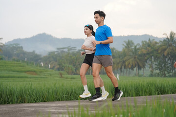 Obraz premium Asian Indonesian Couple Jogging Beside Rice Fields and Tropical Mountain Landscape in Yogyakarta