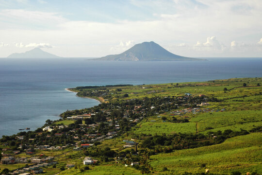 Saint Kitts, the green plain of Saint Kitts, with a small city, on the shores of the caribbean sea, and the volcano of the Netherlands' owned Sint Eustatius Island in the background