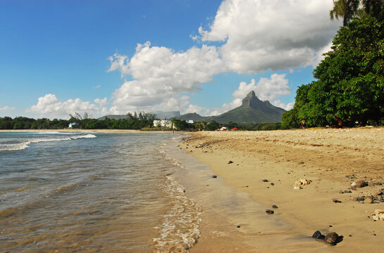 Mauritius, Tamarin, view of calm beach with trees and mountain peak in the background against cloudy sky