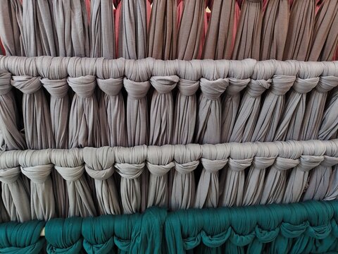 Full frame close-up of soft jersey fabric samples neatly tied and arranged on display racks in grey and emerald green colors for fashion retail or textile manufacturing