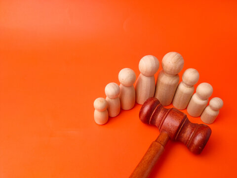 A wooden gavel lies in front of a semicircular arrangement of seven wooden peg figures on orange paper