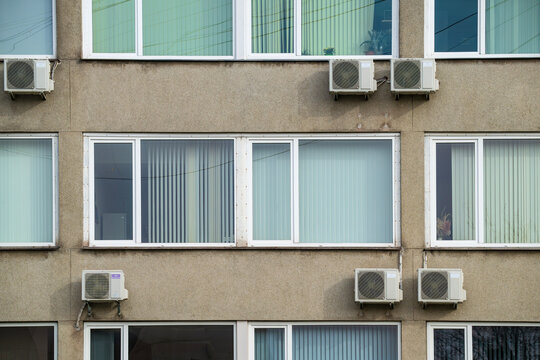 Concrete building facade with office windows, vertical blinds, and air conditioning units mounted on the wall in Talsi, Latvia.