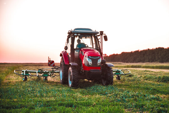 Modern red tractor working with forage harvesting equipment in an agricultural field. Contemporary farm machinery used for efficient hay and forage production.