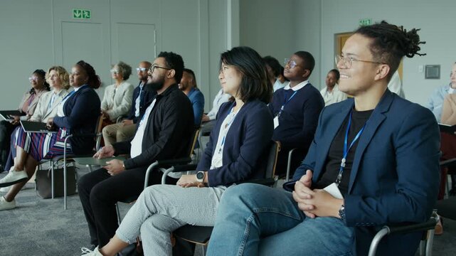 A diverse audience of professionals are attentively listening during a corporate event or seminar. They are focused and engaged, participating in learning and collaboration at a business conference.