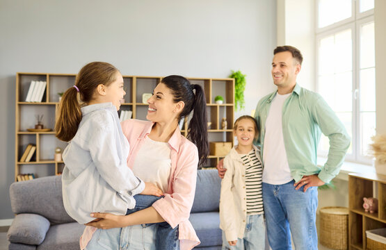 Family parents with daughters smiling at home. Mother lifts younger girl as father hugs older sister in a cozy room, showing playful affection and unity. Joyful family unity concept image.