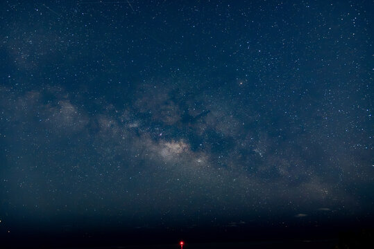 夜空の星々や天の川と海上で赤く光るブイ