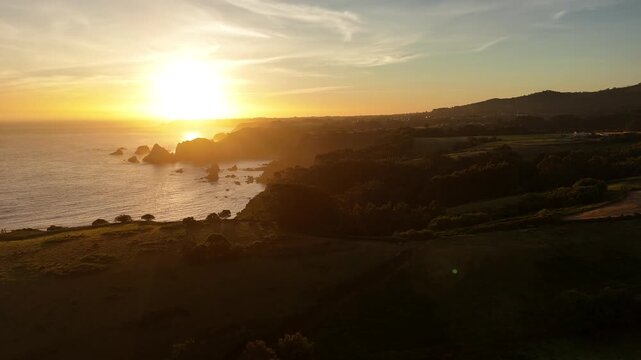 Golden sunset over the rugged Asturian coastline, illuminating offshore rocks, green countryside and the Cantabrian Sea.