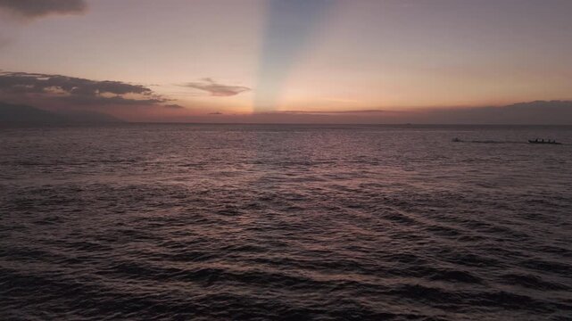 Tropical sea at twilight with warm pastel sky and a long narrow boat moving across the distant horizon.