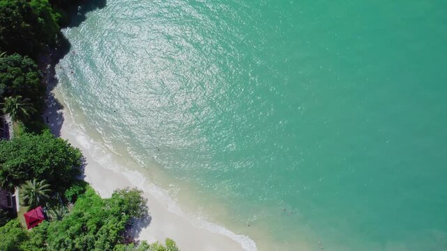 Cinematic top-down drone footage revealing the full expanse of a pristine white sand beach bordered by lush tropical vegetation and crystal-clear turquoise waters in Langkawi, Malaysia.