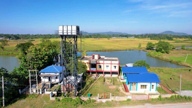 Rural government school campus with classroom buildings, water tower, pond, boundary wall and surrounding farmland highlights education infrastructure in Junbeel, Assam, India, North East India.