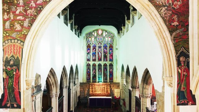 Symmetrical interior view through the medieval Doom Painting arch toward the chancel altar and stained glass window inside St Thomas Church Salisbury